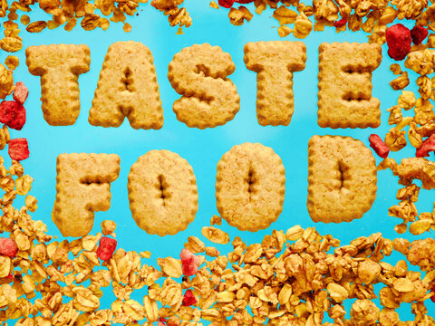 Crispy cereal letters spell 'TASTE FOOD' on vibrant blue surface. Golden flakes and red fruit pieces scatter around. Perfect for food blogs, nutrition content, or breakfast-themed designs