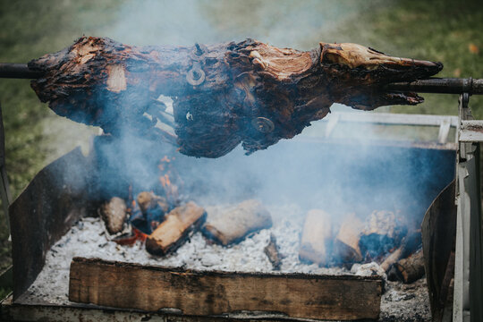 Whole lamb roasting on a spit over an open fire, surrounded by smoke and wooden logs, showcasing traditional outdoor cooking methods in a natural setting