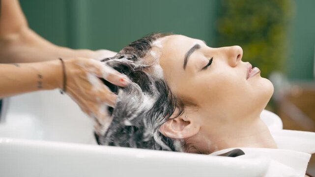 Relaxed young woman receiving a hair wash and scalp massage from a professional hairstylist. Pampering and beauty treatment in a modern salon