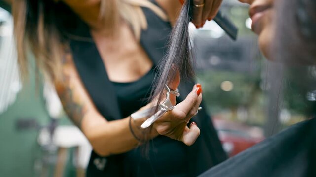 Professional hairstylist trimming the ends of a female client's long, dark hair. Close up on the scissors during the haircut process