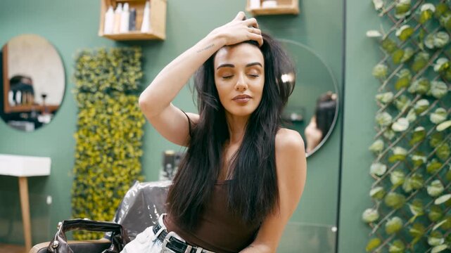 Young gorgeous woman sitting in a modern beauty salon chair. Confident female client with a fresh haircut and hairstyle touching her hair