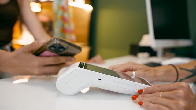 Close up of a customer making a purchase using her mobile phone. The cashier enters the amount on the POS terminal for a quick transaction