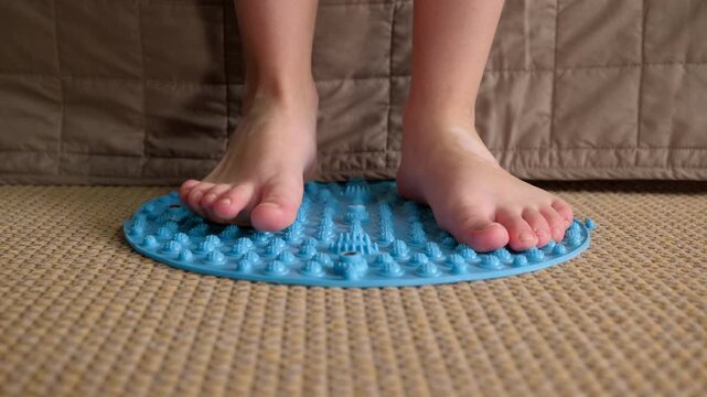 Child performing foot massage on spiked orthopedic mat. Close-up view of a child's bare feet stepping on a spiky mat for a reflexology massage, promoting blood circulation and preventing flat feet
