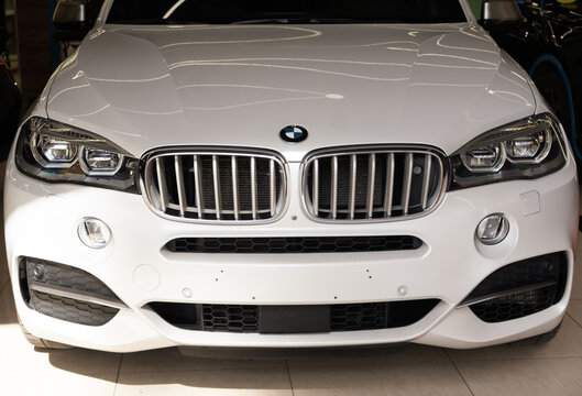 White BMW X5 F15 German luxury SUV car front end close up, passenger crossover automobile bonnet hood with corporate brand round logo badge and chrome double kidney radiator grille inside showroom. 
