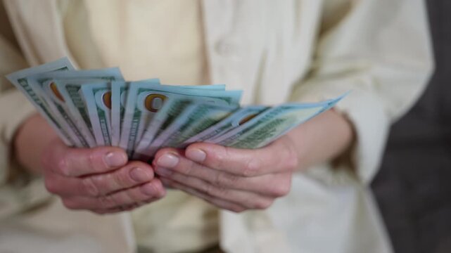Counting hundred dollar bills. Close-up view of female hands counting a stack of one-hundred-dollar bills, neatly fanning them out before securing the cash wad with a black binder clip