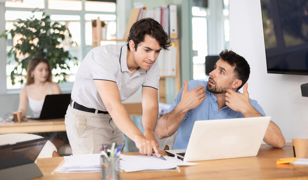 Businessman scolds his employee man sitting at workdesk in the office