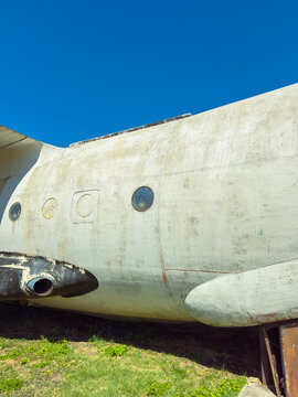 Old airplane fuselage rests on the ground under a clear blue sky at a display site near a museum