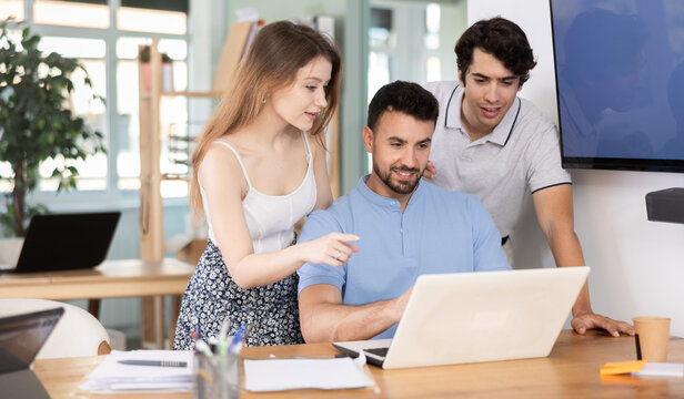Several employees grouped around man colleagues with laptop, heated discussion in office, process of discussion or antecedent interpretation, reasoning. Colleagues monitor dynamics of prices, stock
