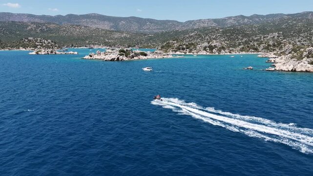 Aerial view of a high-speed Jet Ski creating a powerful wake in deep blue Mediterranean water near a rugged rocky coastline. (Kayalık bir kıyının yakınında, derin mavi Akdeniz suyunda g&uuml;&ccedil;l&uuml; bir su izi