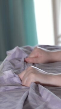 Close up view of a woman's hands nervously gripping and crumpling purple bed linens, symbolizing anxiety, inner struggle, stress, emotional distress, or a disturbing nightmare