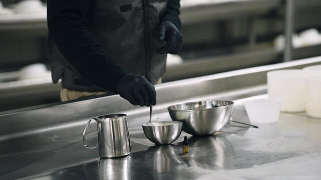 Professional cheesemaker in an artisanal factory preparing ingredients. Worker mixing rennet in a steel bowl to make fresh cheese