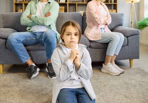Child parents family conflict argument at home. A sad girl sits on the floor as parents sit apart, showing separation, stress, anxiety and trauma. Strong concept of family stress and separation.