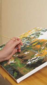 Unrecognizable person engaging in a creative hobby by painting an autumn forest landscape with a brush, a relaxing diy art activity for antistress therapy and mindfulness at home
