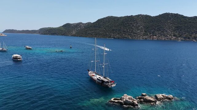 Aerial orbit shot of a traditional Turkish gulet yacht anchored in the turquoise waters of Kalekoy (Simena) near Kekova, Turkey. (Kalek&ouml;y/Simena, Kekova, T&uuml;rkiye yakınlarındaki turkuaz sularda demirle
