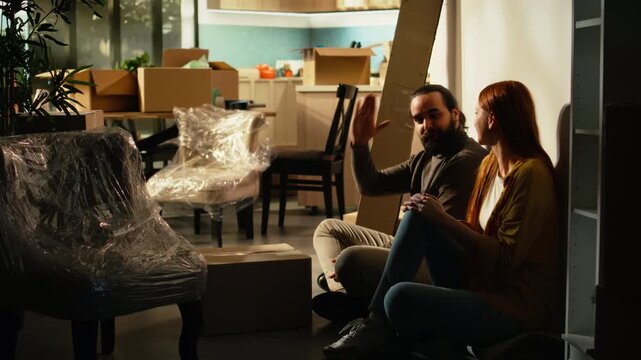 Overjoyed man and woman unpack wrapped decorations from cardboard boxes in a modern home, celebrating a fresh start after moving together into a new house.
