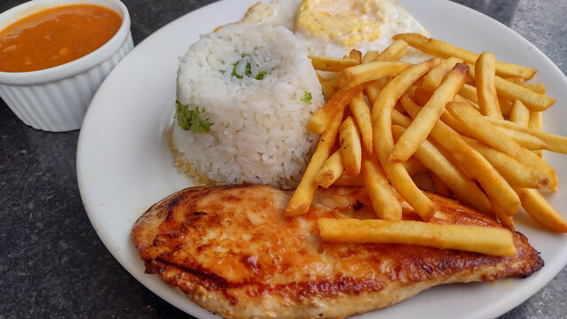 Traditional Brazilian lunch meal called prato feito with grilled chicken fillet, white rice, french fries, fried egg, and brown beans