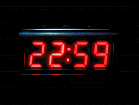 Digital alarm clock displaying the time 22:59 in bright red numbers against a dark background symbolizing late night or impending midnight countdown