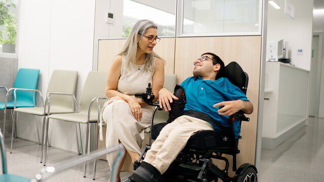 Caregiver and patient with physical disability sharing a moment while waiting in a modern hospital or clinic setting