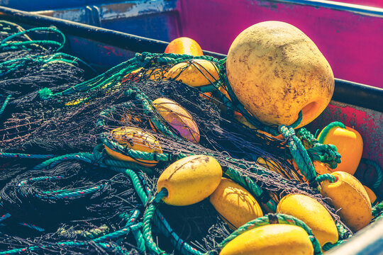 Fishing nets and colorful buoys sit piled in a weathered boat hull. Ropes, floats, and tangled mesh reflect the working gear of coastal fishing industry