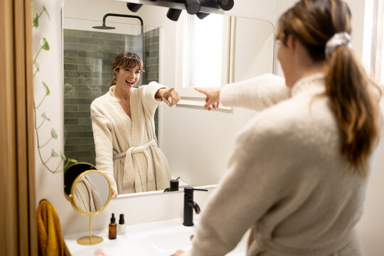 Woman smiling and pointing at her reflection in bathroom mirror