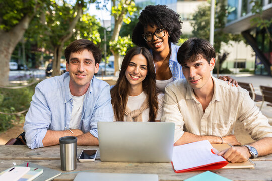 Portrait of a diverse group of happy young business school students looking at camera and smiling outdoors, MBA classmates with laptop on campus. Education concept