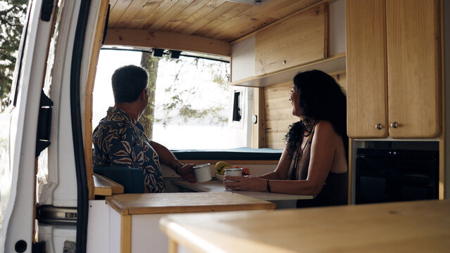 Mature couple relaxing inside a customized camper van, drinking coffee and looking out the window, embracing travel lifestyle