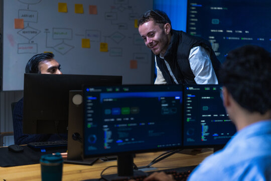 A young male engineer in washed denim concentrating on his screens rests a hand on the mouse while reading through a long log file in a modern data operations centre