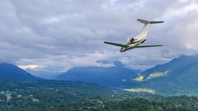 Private Jet Flying Over Lush Mountains And Cloudy Sky Background In British Columbia, Canada