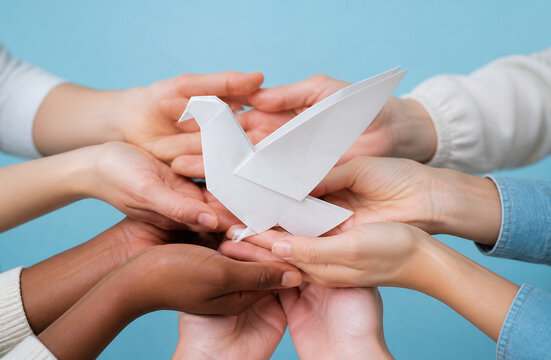 Diverse human hands holding white paper origami dove together against light blue background representing peace unity global support hope and harmony concept stock photo