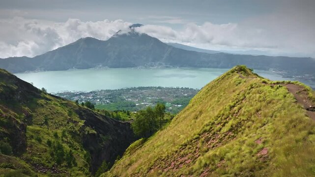 Man standing with arms outstretched on grassy mountain ridge, overlooking the scenic Batur caldera lake and mount Batur volcanoon Bali island, representing freedom and achievement. Aerial drone flight
