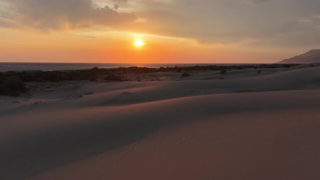 Cinematic forward-moving drone shot over a vast sand dune landscape at sunset by the sea. (Deniz kenarında, g&uuml;n batımında u&ccedil;suz bucaksız kum tepesi manzarası &uuml;zerinde sinematik, ileriye doğru hareket 