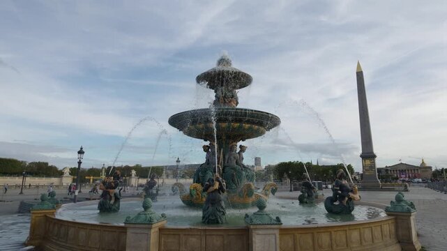 Water spraying from the ornate Fontaine des Mers with Luxor Obelisk under cloudy sky