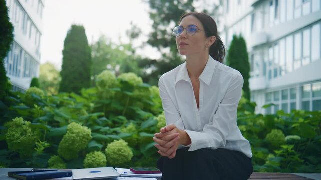 Business professional sits in garden area during work day contemplating tasks and goals