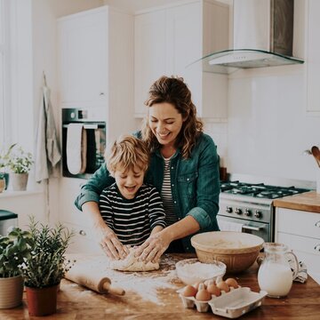 Mother and child baking together in kitchen rolling dough on wooden table