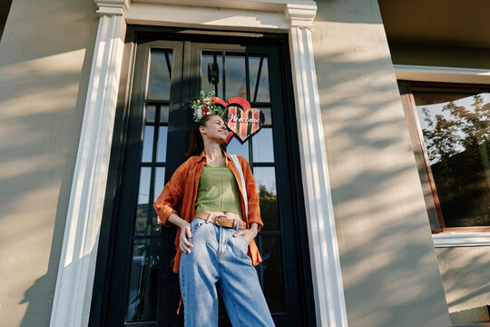 Young woman standing outdoors near a house door. Concept of lifestyle and fashion. Natural lighting creates a warm mood for travel and leisure photography outdoors.