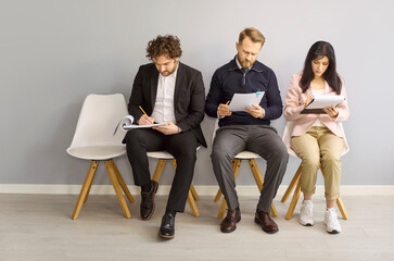 Fototapeta premium Candidates await interview, applicants fill assessment paperwork. In a bright office lobby they wait for recruitment decisions after testing for a vacancy. Clear concept of hiring and talent.