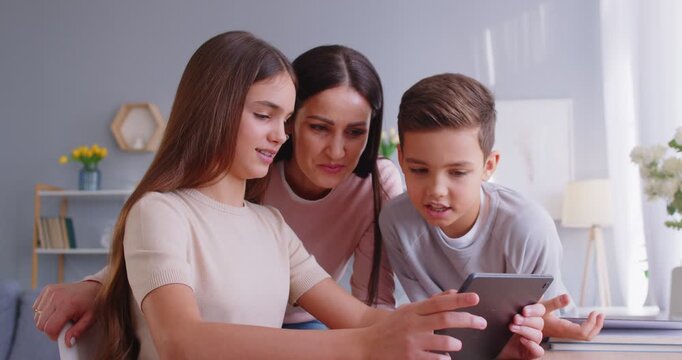 Mother and kids enjoying family leisure time together, using a tablet PC for online entertainment in internet at home. Bonding, technology, and shared activities in a cozy and modern setting.