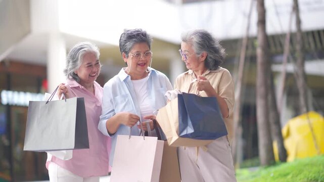 Group of Happy Asian active senior woman travel and shopping at department store in the city. Healthy elderly women friends enjoy and fun urban lifestyle holding shopping bag at shopping mall