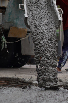 Wet cement pouring from a mixer truck chute onto a steel wire mesh for road