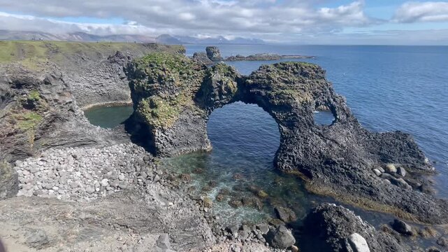 Static view of a natural basalt rock arch on the Icelandic coast, surrounded by rugged volcanic cliffs and the North Atlantic Ocean.