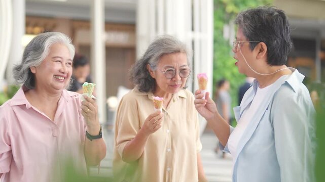 Happy Asian senior woman travel and shopping in the city on summer holiday vacation. Group of Healthy elderly women friends enjoy and fun outdoor lifestyle eating ice cream together at shopping mall.