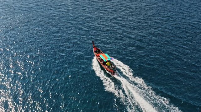 Traditional Thai longtail boat cutting blue ocean, leaving a white wake, serene seascape perfect for tropical escape and adventure. Tourist boat tour near Phuket island. Aerial drone tracking shot