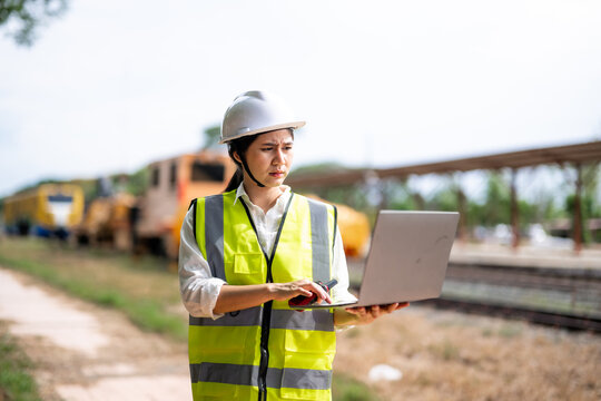 Female Railway Worker in Safety Vest and Hard Hat Using Laptop Near Tracks