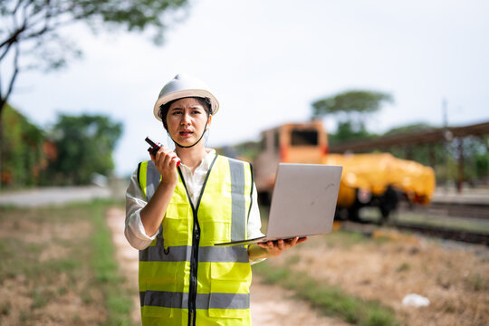 Woman Railway Engineer in Safety Vest and Helmet Using Laptop Near Train Tracks