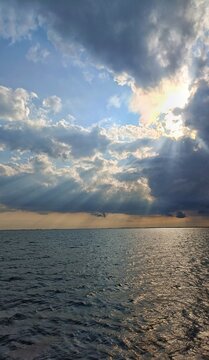 Vertical view of dramatic sky with sunbeams breaking through cumulus clouds over calm ocean horizon