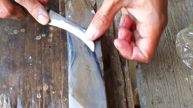 Hands sharpening a curved knife on a wet natural sharpening stone, highlighting traditional blade maintenance.