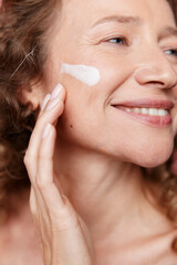 Authentic beauty of a middle aged woman applying face cream, showing natural skin texture without...