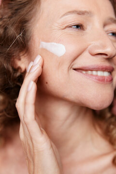 Authentic beauty of a middle aged woman applying face cream, showing natural skin texture without retouching. Concept for skincare, anti aging, and self care routines.