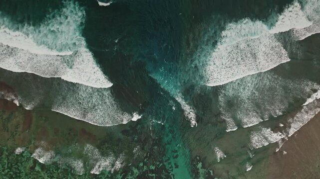 Ocean waves breaking on a vibrant coral reef, revealing clear turquoise water and the dark blue deep sea in Amed, Bali, creating a serene natural landscape and nature background. Aerial top down shot