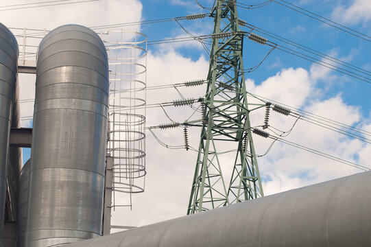 A close-up of a pipeline and a power transmission tower against a blue sky
